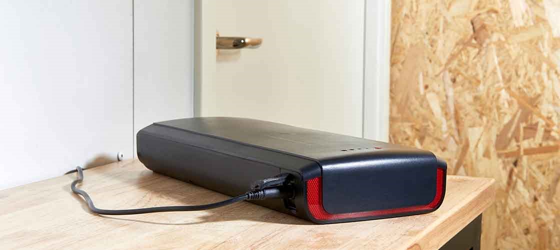 Elcykelbatteri som laddas på en arbetsbänk inomhus.
