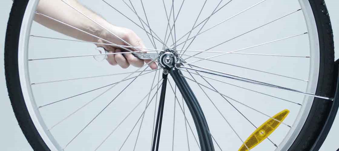 Närbild på en hand som justerar ett cykelhjul med en reflex på.