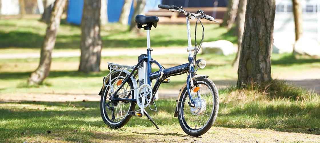 En liten elcykel som står parkerad på en gräsmatta i ett soligt parkområde.