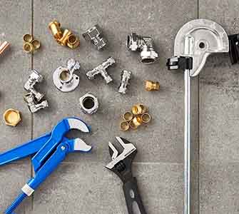 En närbild på olika VVS-kopplingar och VVS-verktyg som ligger utspridda på ett grått stengolv.