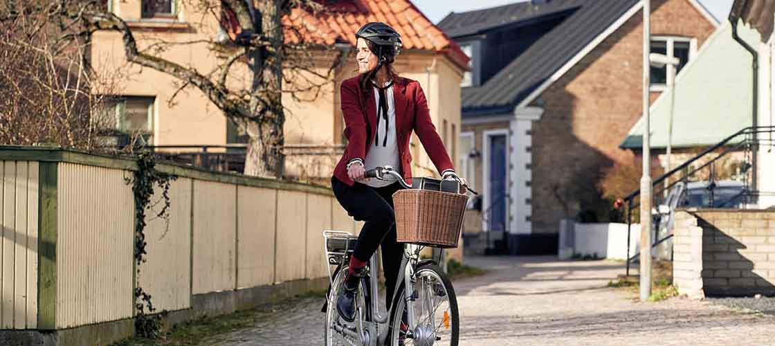 Person med cykelhjälm cyklar längs en solig gata i ett bostadsområde med hus i bakgrunden.
