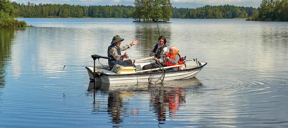 Tre personer sitter i en liten motorbåt och fiskar på en stilla insjö omgiven av träd.